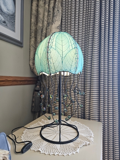 Sea Blue Jellyfish table lamp on a small side table beside patterned curtains in a customer home.